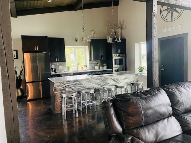 The modern kitchen features dark cabinetry and stainless steel appliances, with a large island adorned by metallic wavy detailing. Barstools are positioned around the island, creating a functional space for dining. Natural light filters through the windows, illuminating the open layout.