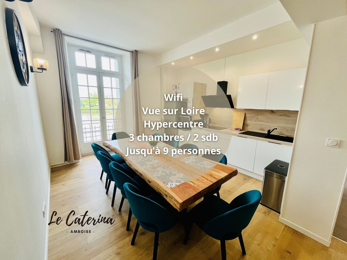 A spacious dining area features a large wooden table surrounded by blue upholstered chairs, ideal for gatherings. The open kitchen is equipped with modern cabinetry and appliances, creating a functional space. Natural light streams through large windows, enhancing the inviting atmosphere.