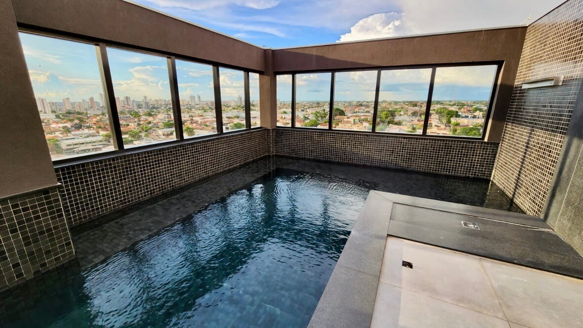 A rooftop pool is featured with expansive windows offering panoramic city views. The pool's surface reflects sunlight, and tiled walls create a modern aesthetic. The surrounding area is finished with sleek stone surfaces, enhancing the overall sense of spaciousness and tranquility.