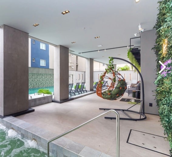 An inviting leisure area is visible, featuring a hanging chair surrounded by lush greenery. Contemporary loungers are arranged alongside a tranquil pool, offering a soothing escape. Large windows create an airy ambiance, allowing natural light to fill the space.