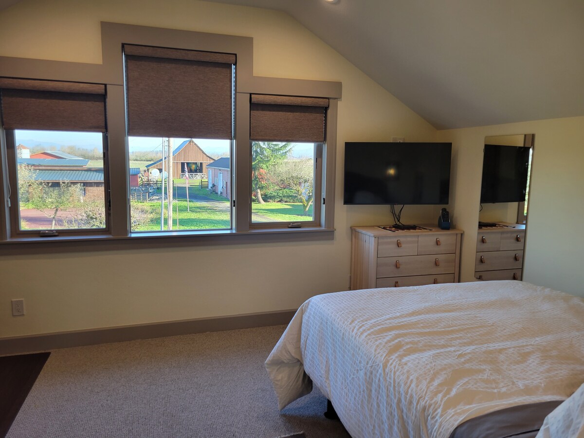 Ხედი საძინებლიდან აღმოსავლეთისკენ.  Საძინებელში არის საწოლი, ტელევიზორი, მაგიდა, კარადა, ჟალუზები დამატებითი უშუქო ფანჯრების ფერებით და ზღაპრული ხედი ფერმერულ აქტივობებზე.