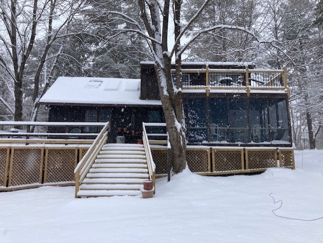 The exterior of a classic cabin is shown, surrounded by snow-covered trees. The deck features a railing and stairs leading to a warm, enclosed porch. Snowflakes gently fall over the scene, while the cabin blends smoothly into its peaceful, wintry setting.