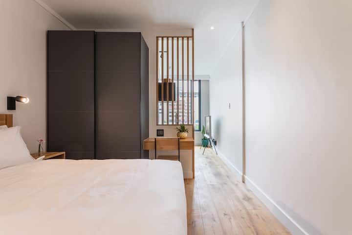 Apartamento tipo estudio. La sala de estar y el dormitorio están separados por la cocina y las vigas de madera. Pero la sala de estar tiene cortinas y persianas para bloquear la luz.