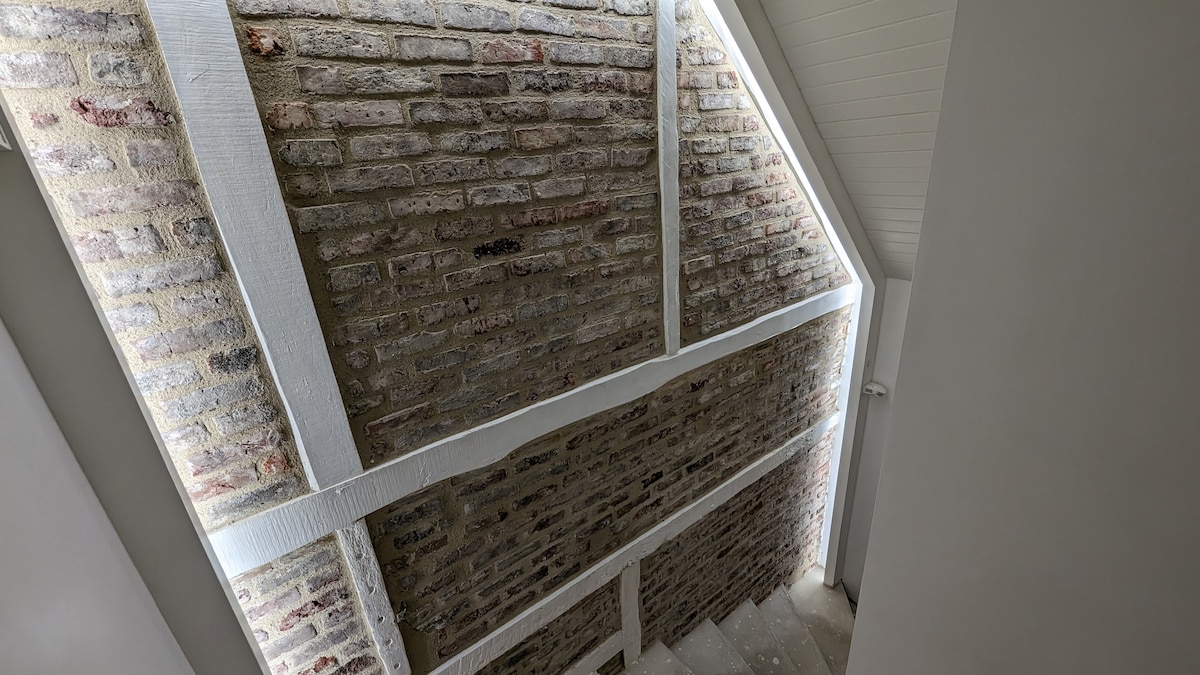 A well-lit staircase is featured, showcasing exposed brick walls and wooden beams that highlight the architectural detail. Soft lighting enhances the natural textures, while the open space creates a welcoming feeling as one ascends to the upper level.