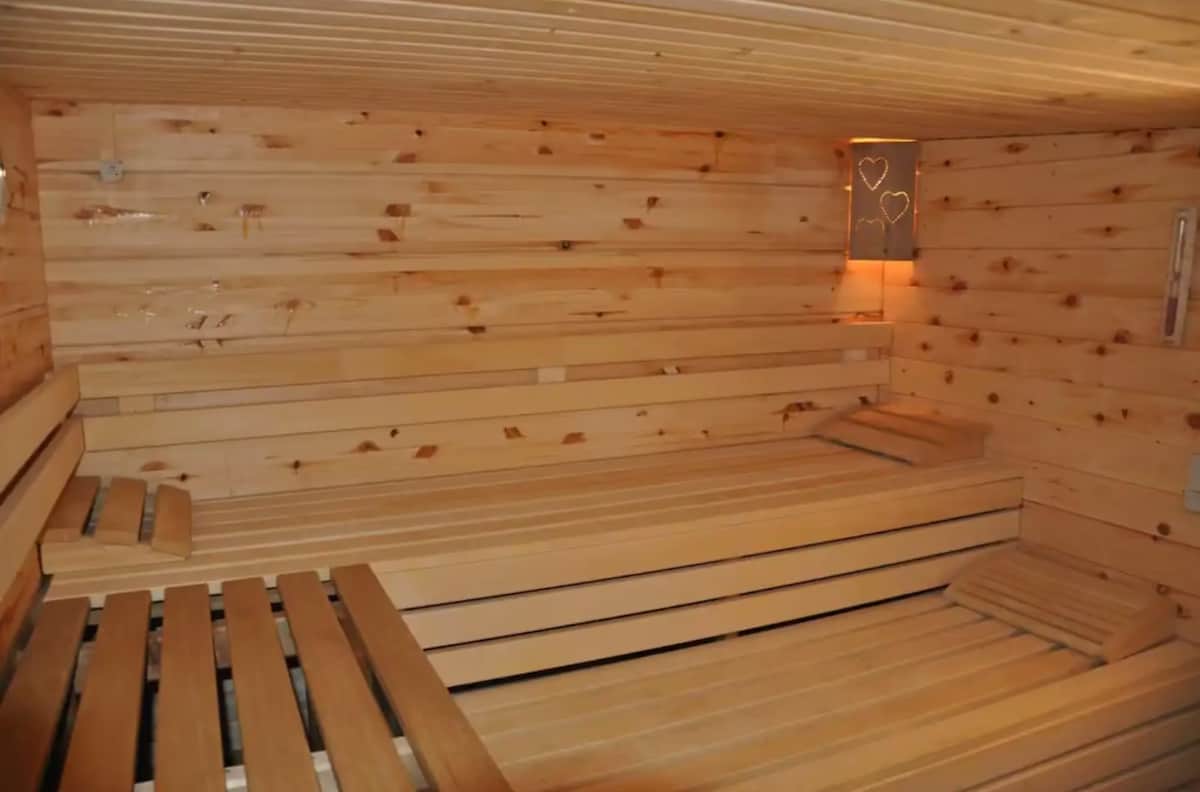 A wooden sauna interior is showcased, featuring light-colored wooden benches arranged for relaxation. The walls are lined with smooth, pale wood, and soft lighting creates a warm ambiance. A decorative element with hearts is visible, providing a subtle detail.
