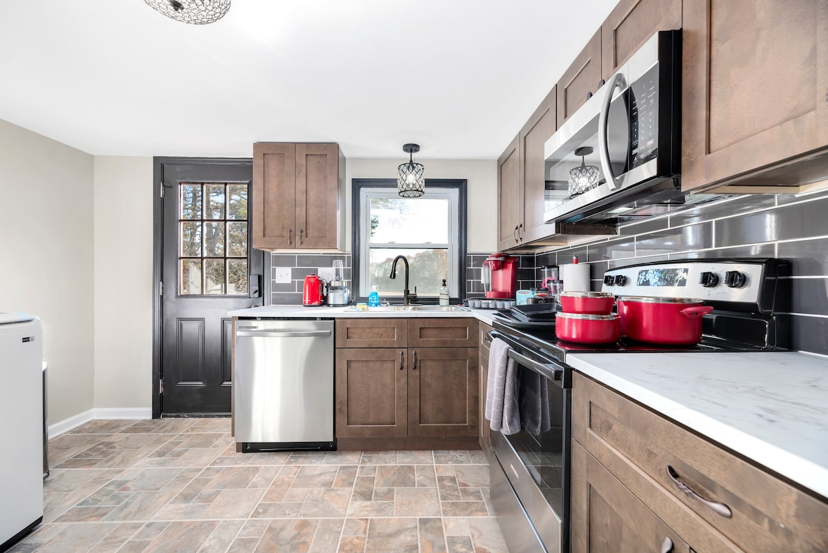 The kitchen features modern cabinetry with dark wood finishes and a stylish tile floor. Stainless steel appliances are set against a black backsplash, while red cookware adds a pop of color. Natural light floods through a window, enhancing the functional workspace.