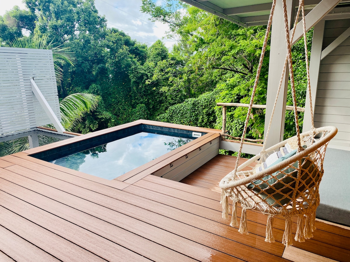 A private pool is nestled among lush greenery, surrounded by a wooden deck that enhances the natural setting. A cozy swing chair is positioned nearby, inviting relaxation and enjoyment of the serene environment.