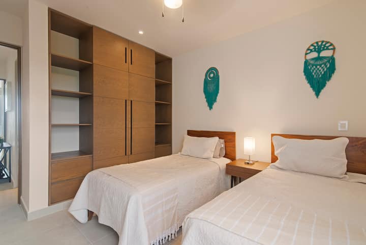 Zweimal der Komfort, doppelt so charmant. Unser gemütliches Schlafzimmer verfügt über zwei einladende Betten mit bequemen Bettlaken und Kissen, gepaart mit einem geräumigen Wandschrank für stilvolle Kleiderschrankaufbewahrung. Erlebe den Luxus erholsamer Nächte und organisierter Eleganz.