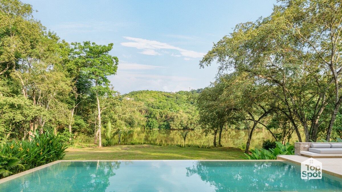A tranquil pool reflects the surrounding greenery, offering clear views of the water and lush foliage. The scene is complemented by the distant hills and a serene sky, creating an inviting atmosphere for relaxation and outdoor enjoyment.