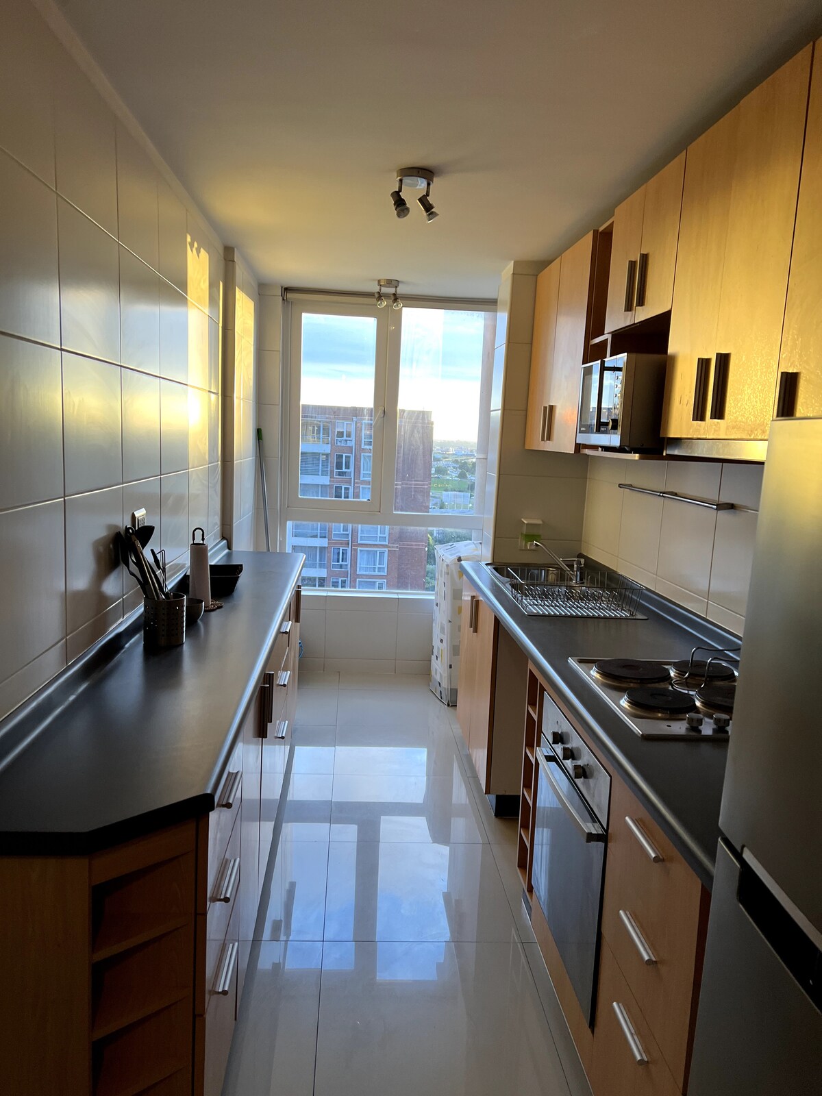 A modern kitchen design features sleek cabinetry and stainless steel appliances. Natural light filters through a large window, illuminating the countertops. A minimalist layout is observed with essential cooking tools neatly arranged, creating a functional cooking space.