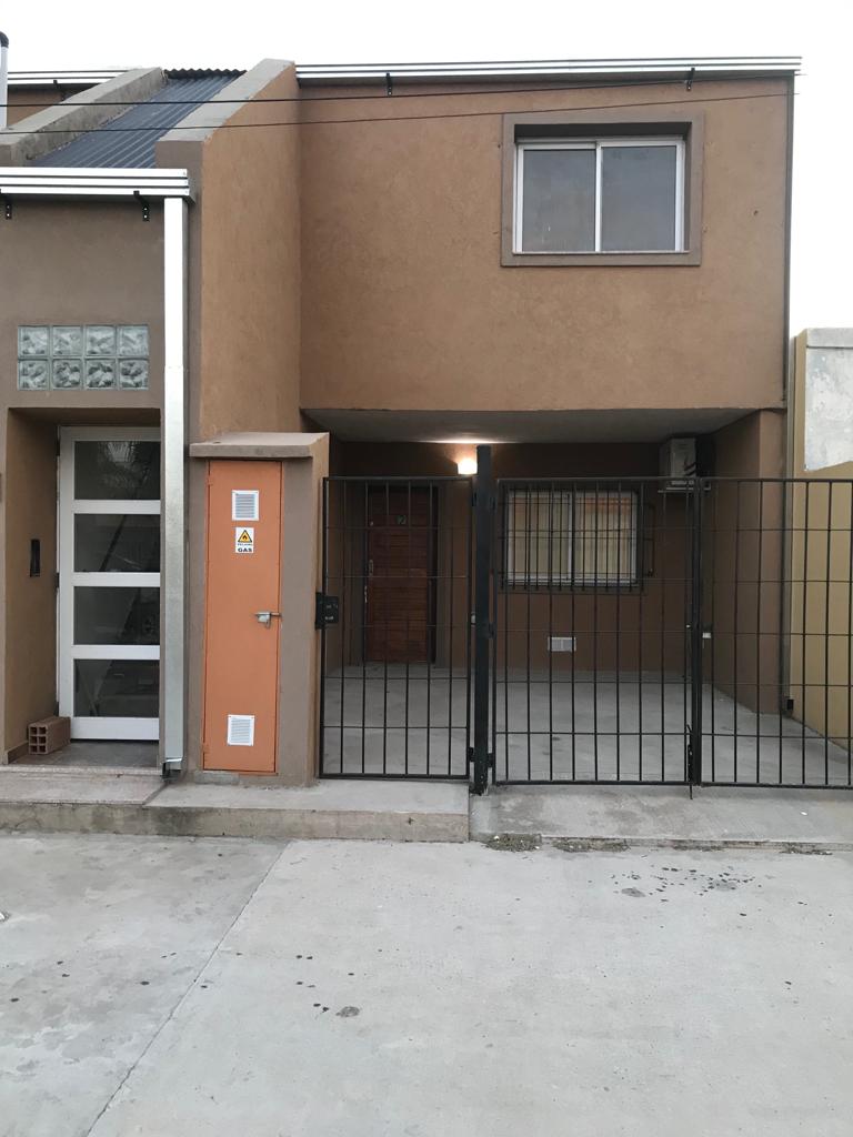 The exterior of the building features a two-story structure with a neutral-colored facade. A gated entrance provides security, while a front porch area is visible. A small window is located on the upper level, allowing natural light into the space.