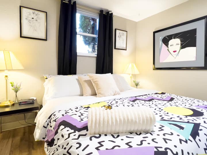 Retro bedroom featuring a plush king bed, iconic 80s Patrick Nagel artwork, and warm, cozy lighting and black out curtains. A stylish, design-focused space perfect for relaxing and enjoying a truly unique themed stay.
