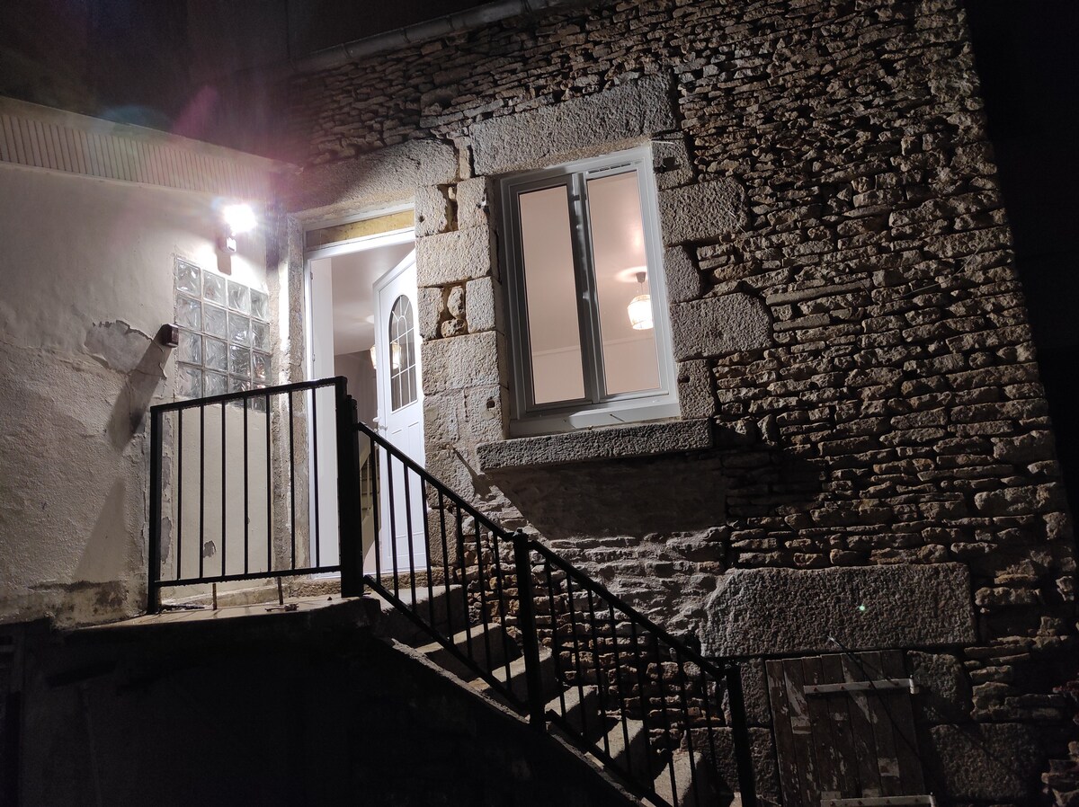 The image depicts a two-story entrance featuring a stone exterior. A white door is framed by a glass block window, and a porch light illuminates the area. A set of stairs with a metal railing leads up to the entrance.