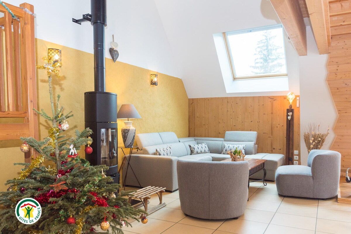 A living area features a cozy seating arrangement with a fireplace. Natural light enters through a large skylight, illuminating the warm walls. Decorative elements, including a Christmas tree, add a festive touch to the space, while the wooden accents enhance its rustic charm.