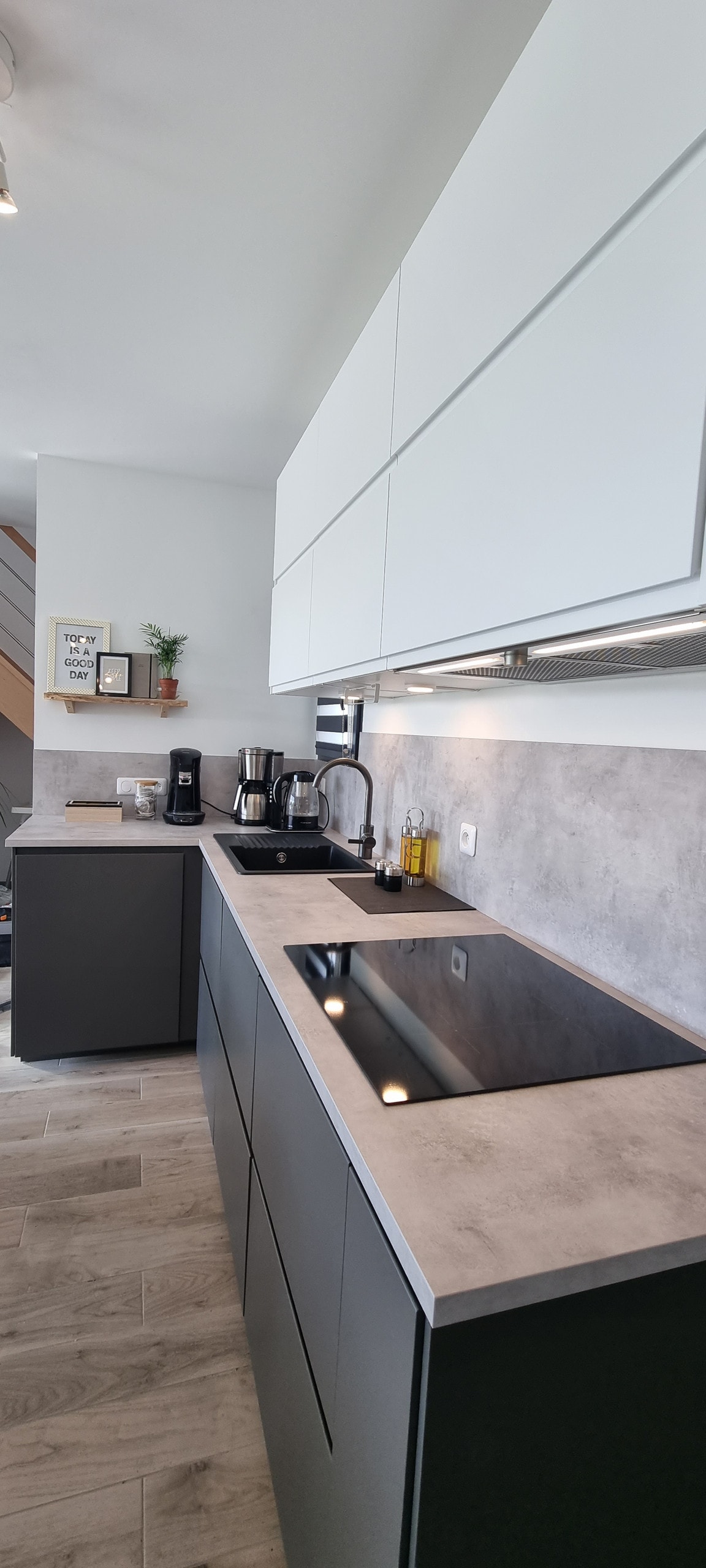 A modern kitchen is featured, equipped with sleek cabinetry in neutral tones. A dark countertop contrasts with the light cabinetry, and appliances are neatly arranged, including a coffee maker and other kitchen essentials. Ample counter space invites meal preparation.
