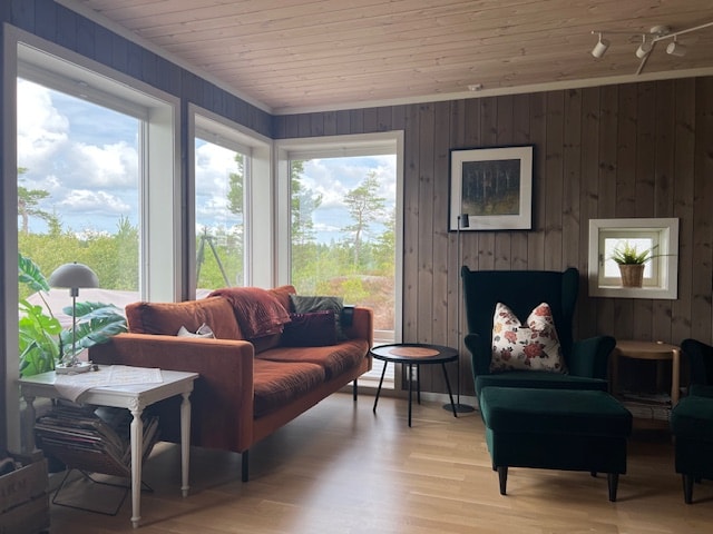 A cozy living area features a comfortable orange sofa and two green armchairs, inviting relaxation. A round table sits nearby, with natural light streaming through large windows showcasing views of surrounding greenery and a distant landscape.