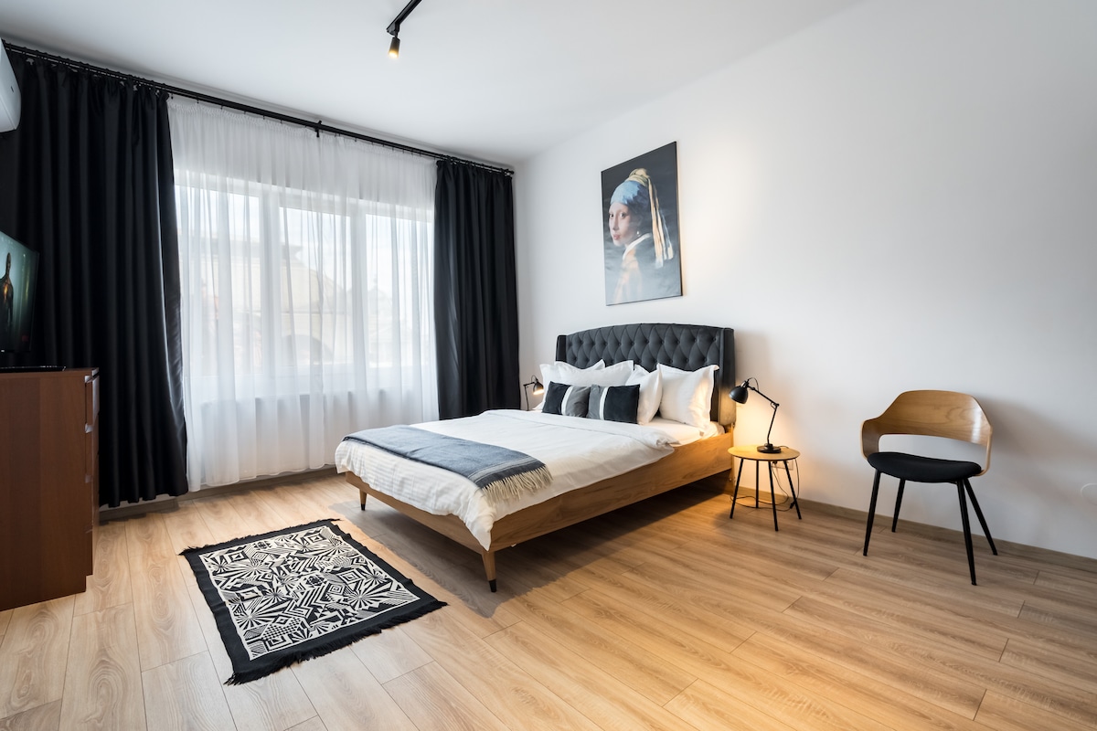 მზით განათებული საძინებელი რბილი, რუხი გადასაფარებლით, ელეგანტური პორტრეტი და იატაკიდან ჭერამდე ჩამოშვებული ფარდები. თბილი ხის იატაკი და მყუდრო სავარძელი ქალაქის ამ ელეგანტურ საცხოვრებელში დასვენებისკენ იწვევს.