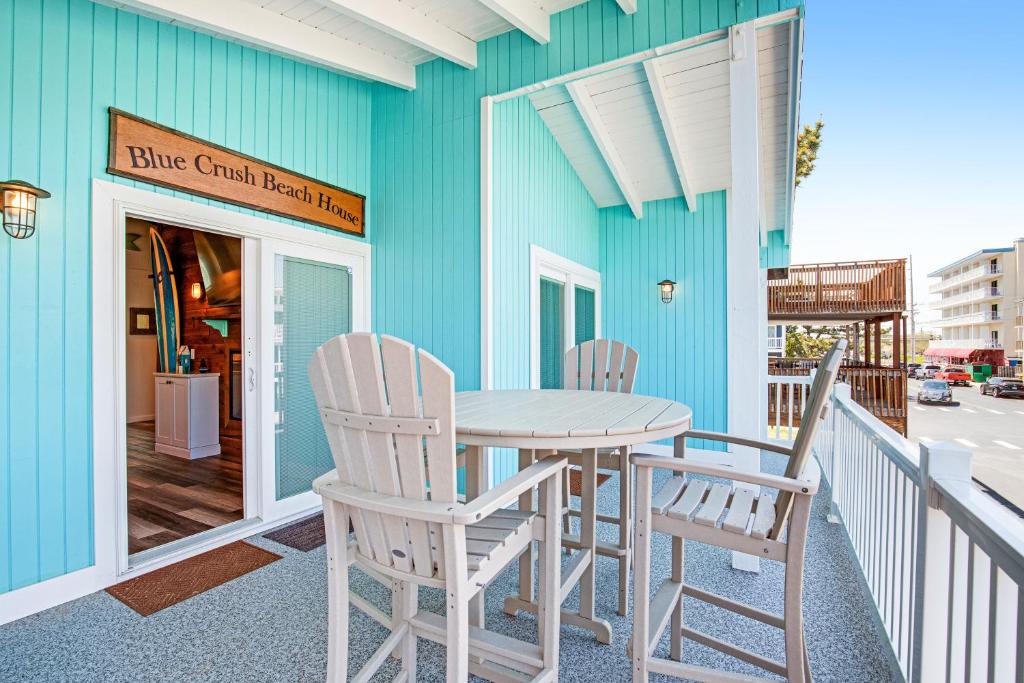 A deck area showcases a round table surrounded by high-backed chairs, all crafted from light-colored wood. The bright blue walls of the beach house create a cheerful atmosphere, while sunlight filters in, highlighting the inviting outdoor space.