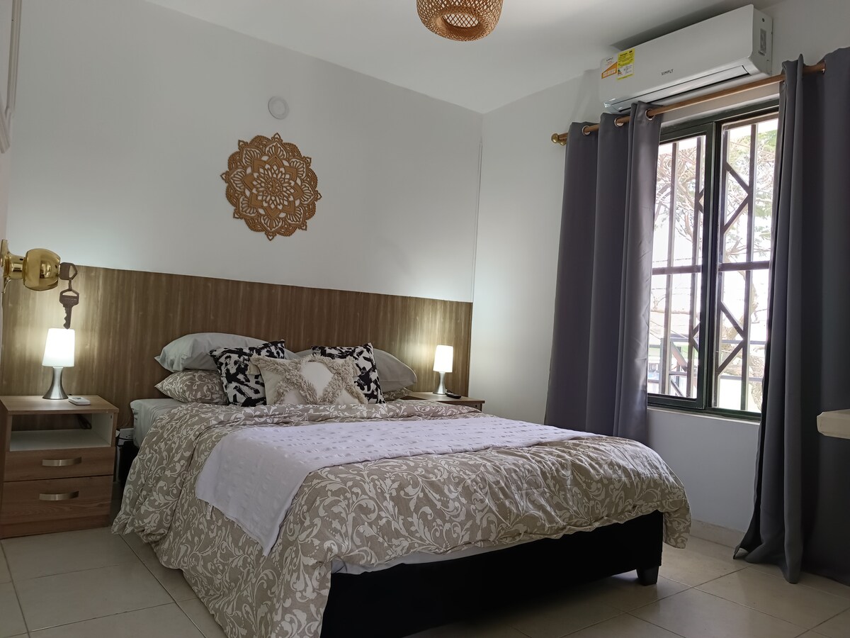 Priestranná hlavná spálňa s manželskou posteľou, klimatizáciou, 32-palcovou inteligentnou televíziou (Netflix, Prime a Crunchyroll), otvoreným šatníkom, zrkadlom, trezorom, pracovným stolom, drevenou nástennou výzdobou, zatemňovacími závesmi a dostatkom prirodzeného svetla.