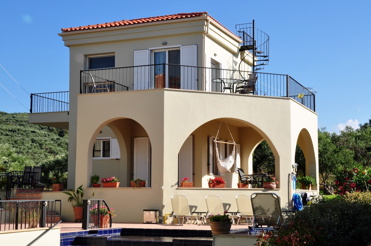 The two-story Guest House features a spiral staircase leading to a private roof terrace. Arched facades and large windows provide a spacious feel, while colorful flower pots enhance the outdoor living areas with ample seating options along the pool terrace.