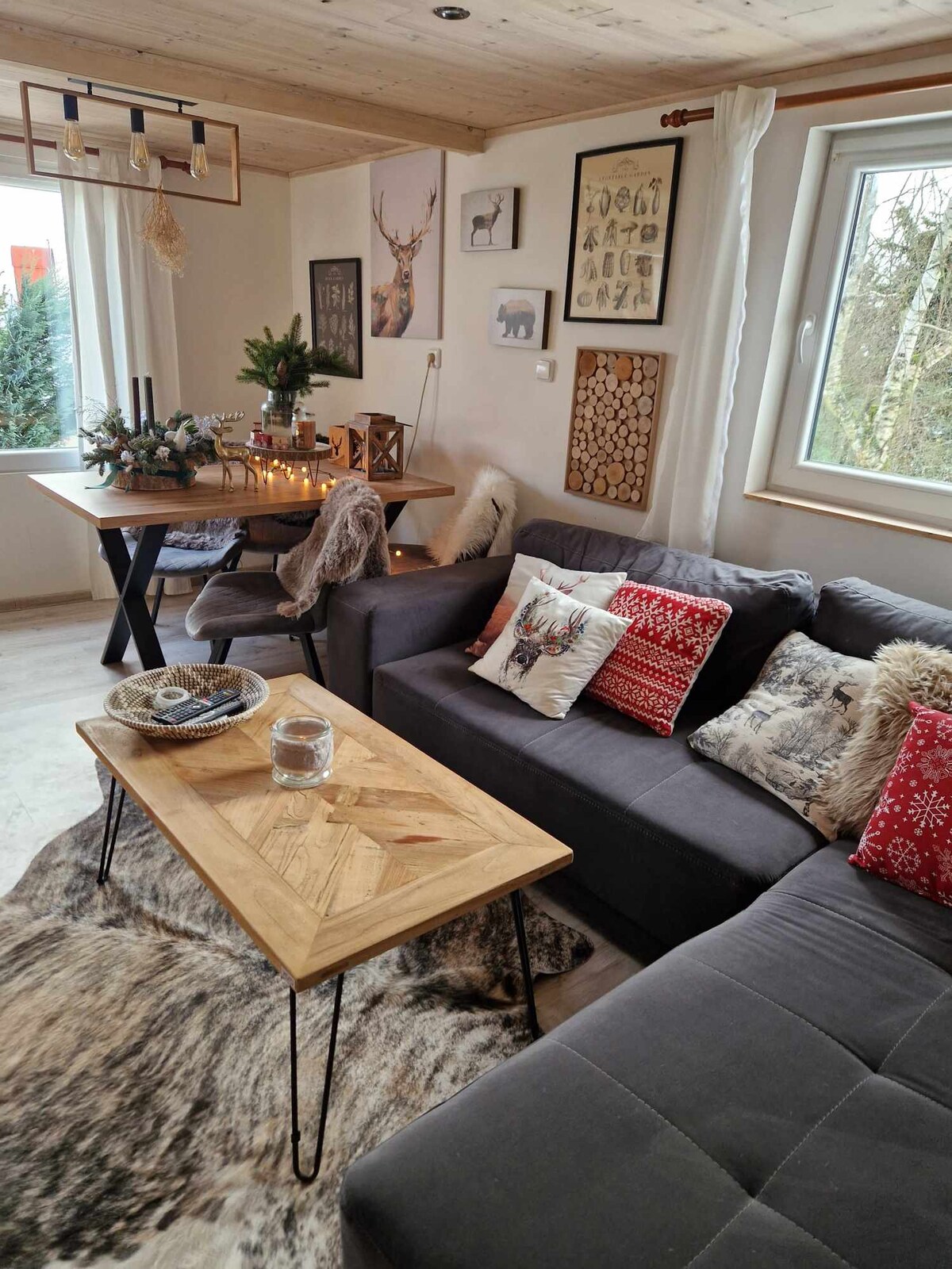 The living area features a cozy sectional sofa adorned with decorative pillows, complemented by a wooden coffee table. A dining table sits nearby, surrounded by candles and greenery. Natural light filters through a window, enhancing the relaxed, inviting atmosphere.