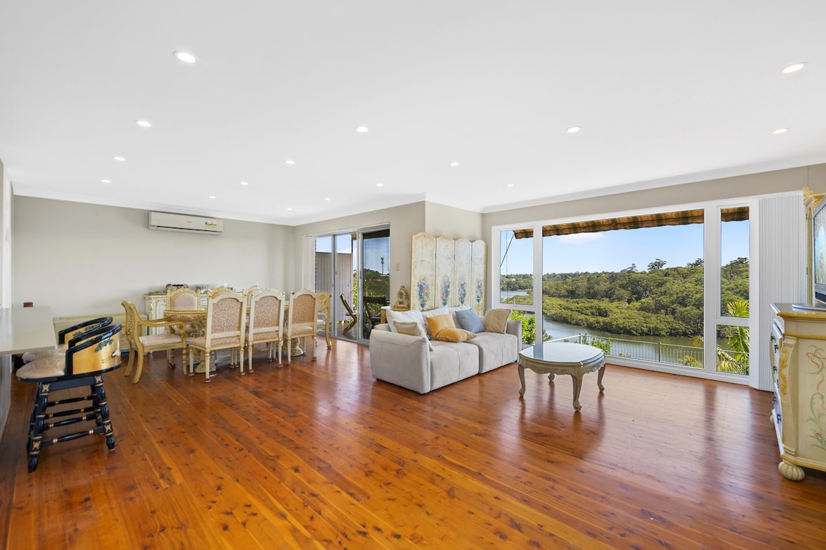 A spacious living area features timber floorboards and large windows that offer views of the Lane Cove River. A comfortable couch and elegant dining set create an inviting space for relaxation and gatherings. Natural light brightens the room, enhancing the overall ambiance.