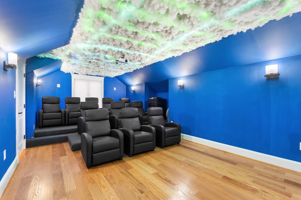 A private movie theater features 11 fully reclining seats arranged for optimal viewing. The ceiling is adorned with a decorative cloud design, and vibrant blue walls enhance the immersive experience. Wood flooring adds warmth to the space, inviting relaxation during movie nights.