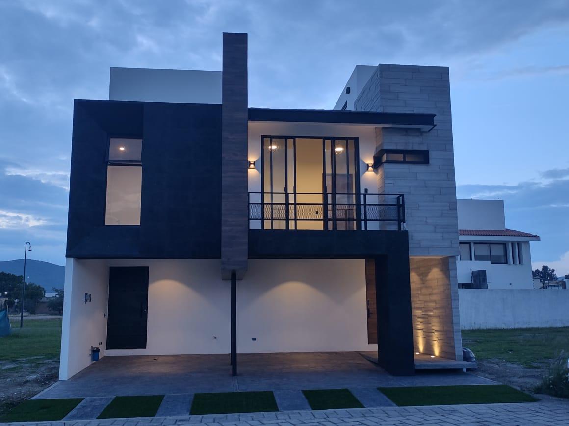 The modern exterior of the property showcases a combination of sleek dark and light tones. Large glass doors prominently feature the entrance, while strategically placed lighting highlights architectural details. A spacious patio area is visible, complementing the overall contemporary design.