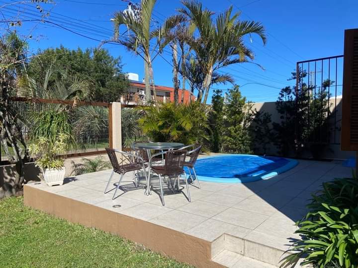 A serene outdoor patio area is featured, complete with a small pool and round dining table surrounded by four wicker chairs. Lush greenery and palm trees provide a tropical ambiance, with a clear blue sky in the background enhancing the inviting setting.