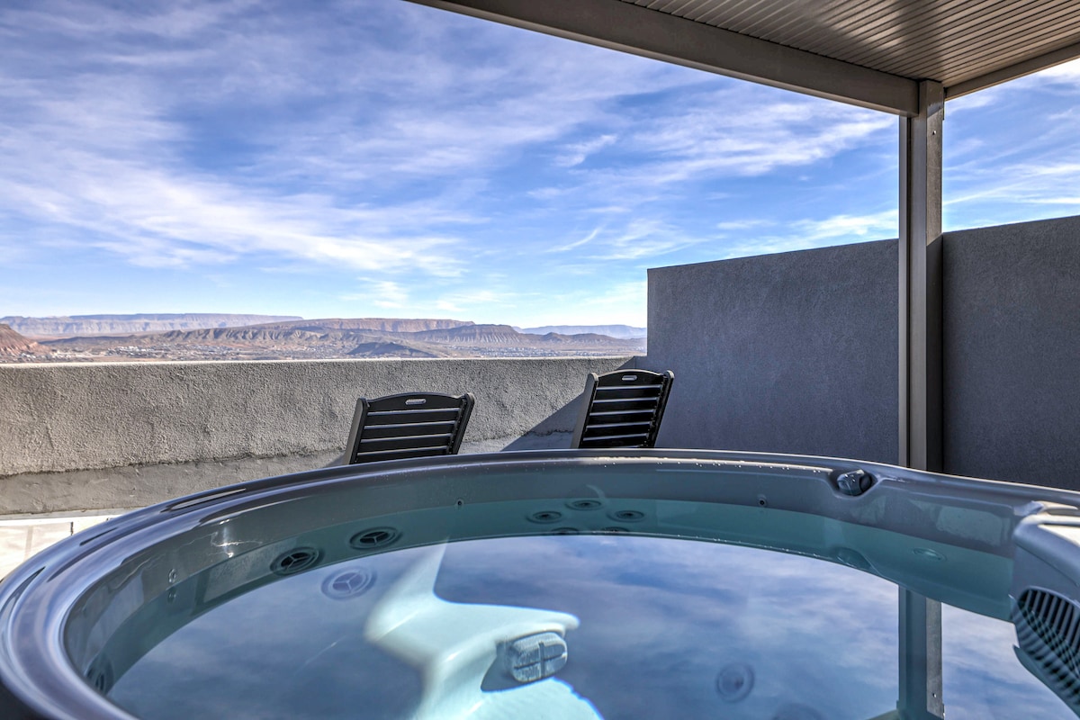 A hot tub is positioned on an upper sky deck, offering expansive views of the desert landscape and distant mountains. Two black chairs are visible beside the tub, providing a space for relaxation while enjoying the scenic surroundings.
