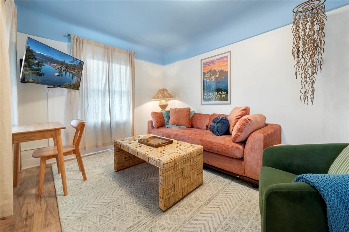 The living area features a vibrant peach sofa complemented by decorative pillows and a cozy green armchair. A wooden coffee table rests on a patterned rug, while a small dining table with a chair is positioned near the window, allowing natural light to brighten the space.