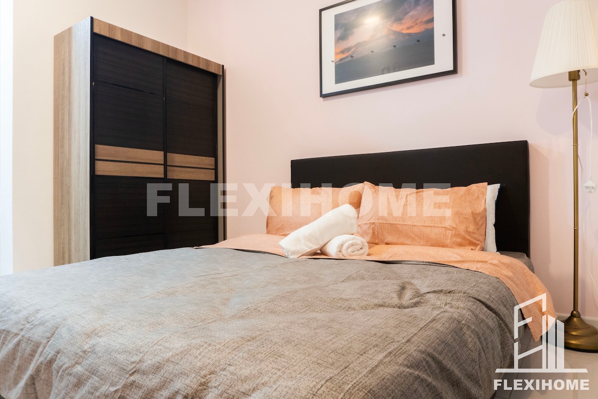 A well-arranged sleeping area features a cozy bed with soft linens. A dark wood wardrobe stands beside the bed, and a framed photograph decorates the wall above. A standing lamp provides gentle light, enhancing the tranquil ambiance of the space.