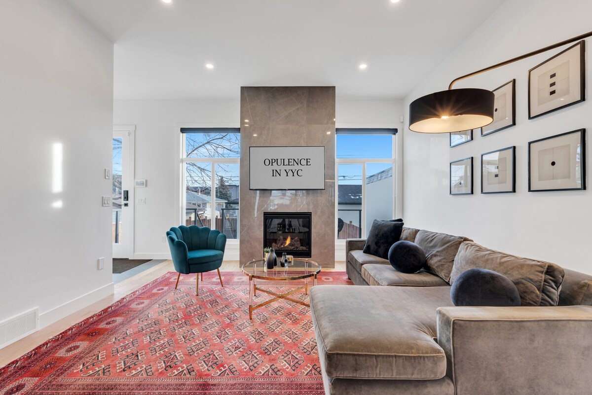A modern living area features a plush sectional sofa and an elegant coffee table. A decorative rug covers the floor, and a fireplace sits within a stylish stone wall. Large windows allow natural light to brighten the space, enhancing its contemporary design.