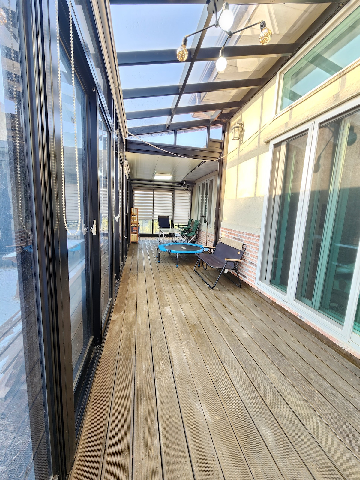 A spacious terrace is shown, featuring wooden flooring and large glass doors that allow for ample natural light. Several lounge chairs and a folding bed are arranged along the side, creating an inviting space for relaxation.