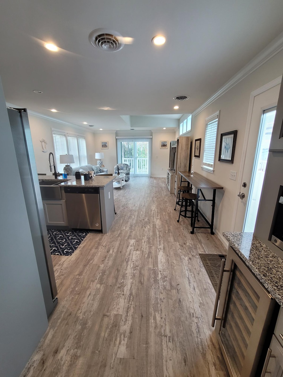The kitchen features modern appliances and granite countertops, with an open layout leading to a bright dining area. Natural light enters through the windows, illuminating the space. A doorway opens to an outdoor area, with stylish bar seating visible in the foreground.
