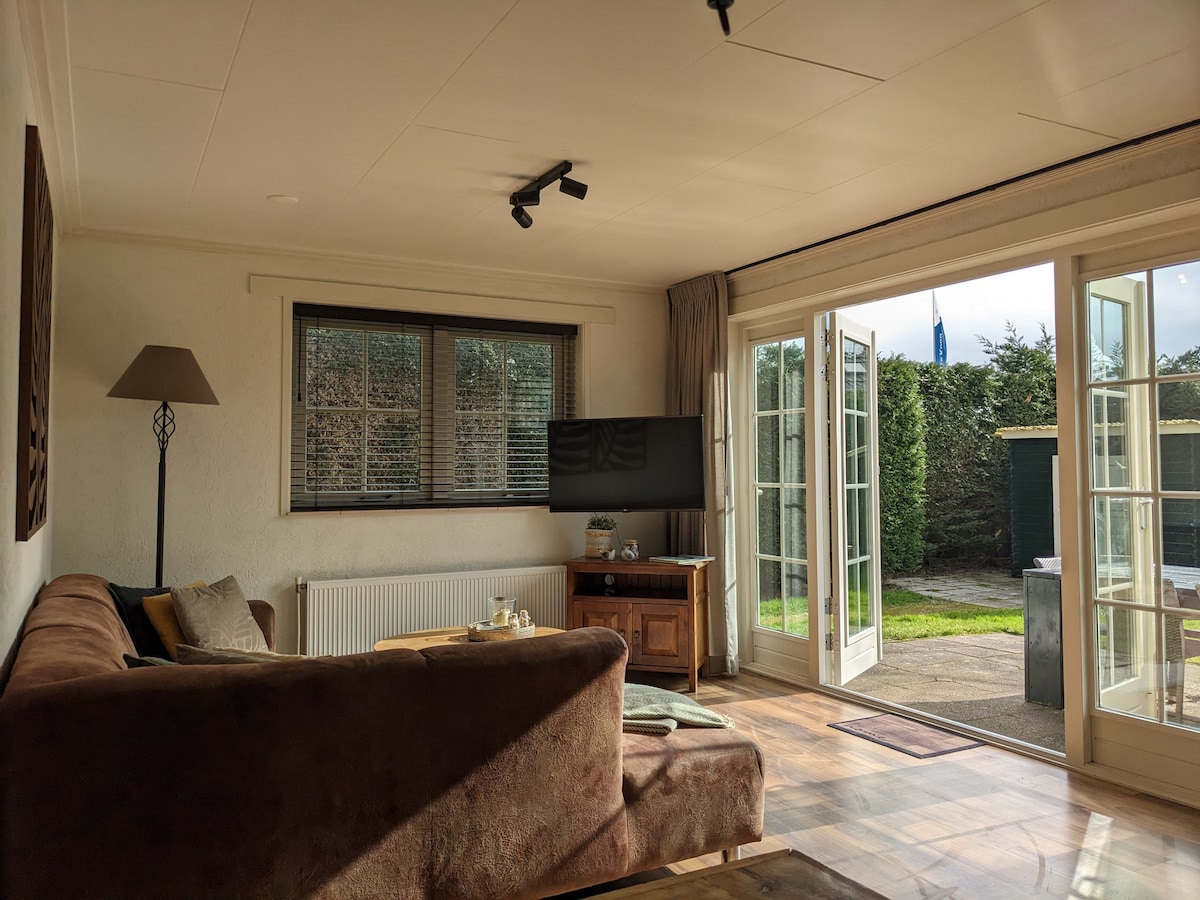 A comfortable living space is presented with a cozy brown sofa and a wooden coffee table. Natural light enters through large, French doors that provide access to the garden. A modern television is mounted on the wall, contributing to the relaxed ambiance.