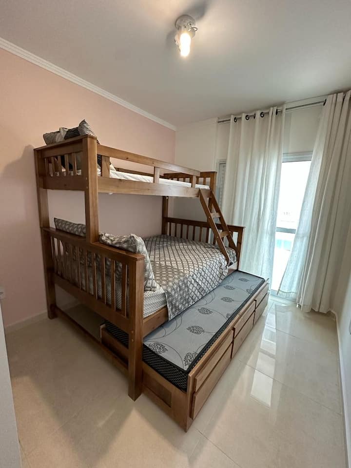 ห้องนอนพร้อมเตียงคู่ เตียงสองชั้นพร้อมเตียงเสริม เครื่องปรับอากาศ และระเบียงที่มีวิวทะเลและภูเขา