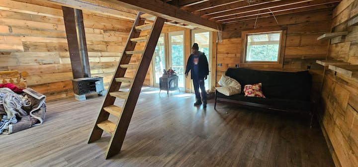 Cabin interior with wood walls, stairs to sleeping loft, and futon