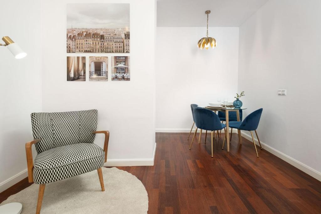 A cozy seating area is visible, featuring a patterned armchair positioned on a round rug. A small dining area is seen in the background, showcasing a circular table accompanied by four blue chairs. Light is provided by a decorative pendant light above the table.