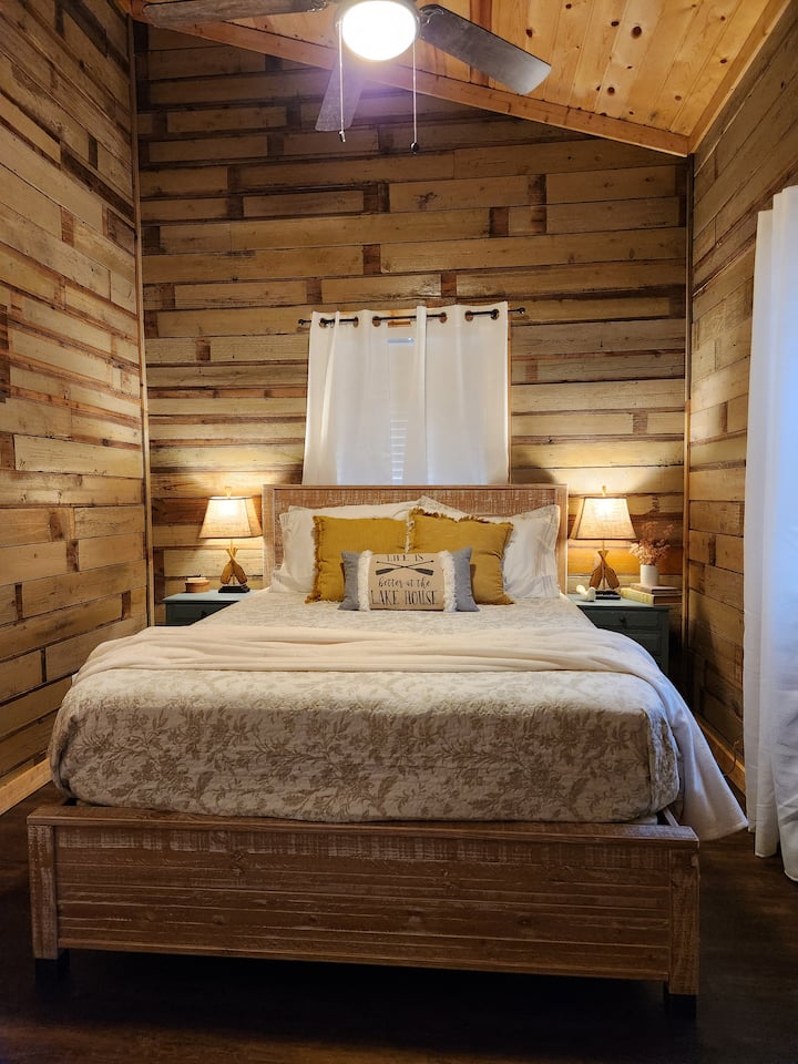 The cabin vibe is strong with this one! This bedroom is in the main house and directly adjacent to a bathroom with tub. All bedrooms come with ROKU TV, ceiling fan, luggage rack and USB charging access at the bedside table