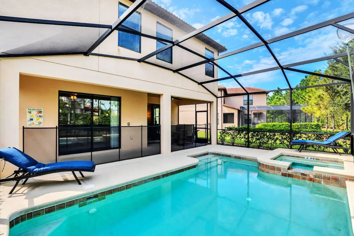 An inviting screened-in patio features a private pool and spa, with a clear blue water surface reflecting the sky. Two lounge chairs are positioned nearby, offering a relaxing area. Greenery surrounds the space, providing a sense of tranquility and privacy.