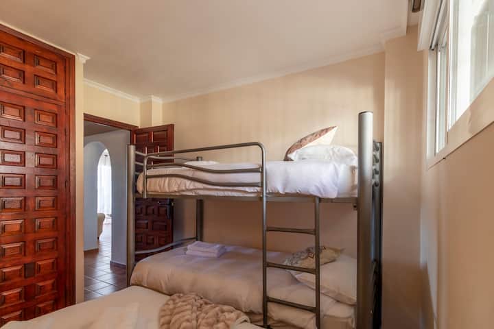 Bedroom with metal bunk beds, white linens and towels, wooden fitted wardrobe, window with blind and ceramic floor. Functional and simple space with access to other rooms.