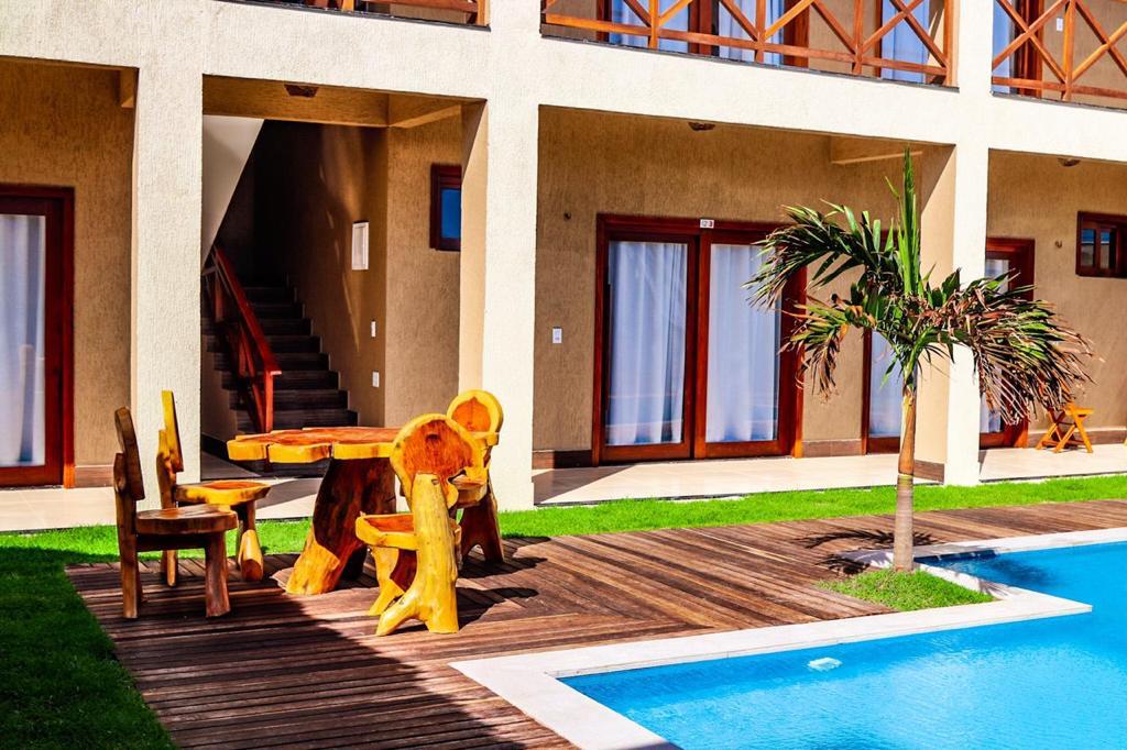 An outdoor area is presented, featuring a wooden table and chairs crafted from natural materials. The space is surrounded by lush green grass and is adjacent to a swimming pool. Large glass doors in the background provide access to the accommodations.