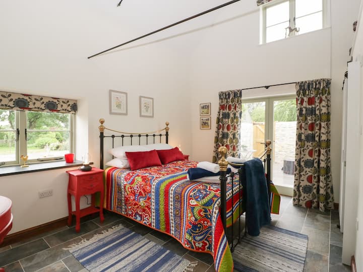 Спална соба со брачен кревет од ковано железо, кревет во стилот на Викторија. Капсулата во бањата со лизгачка врата во стилот на штала е во близина.