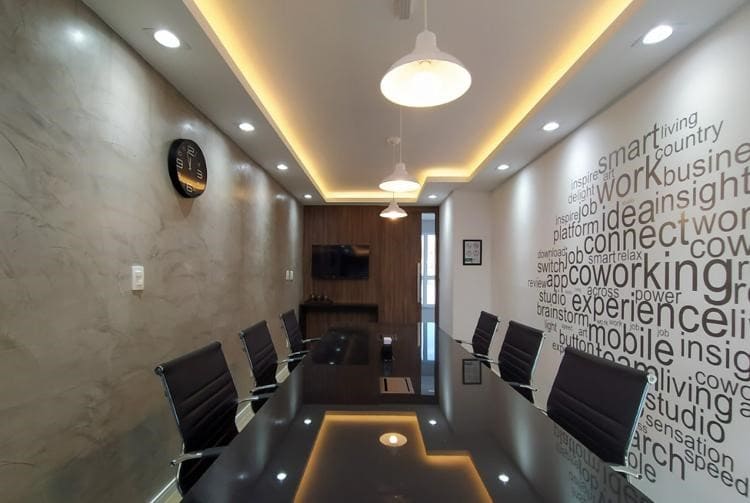 A modern conference room is presented with a large black table surrounded by eight sleek, black chairs. Warm lighting is provided by ceiling fixtures, and a clock is mounted on the wall. Inspirational words are displayed in a creative design along one side.