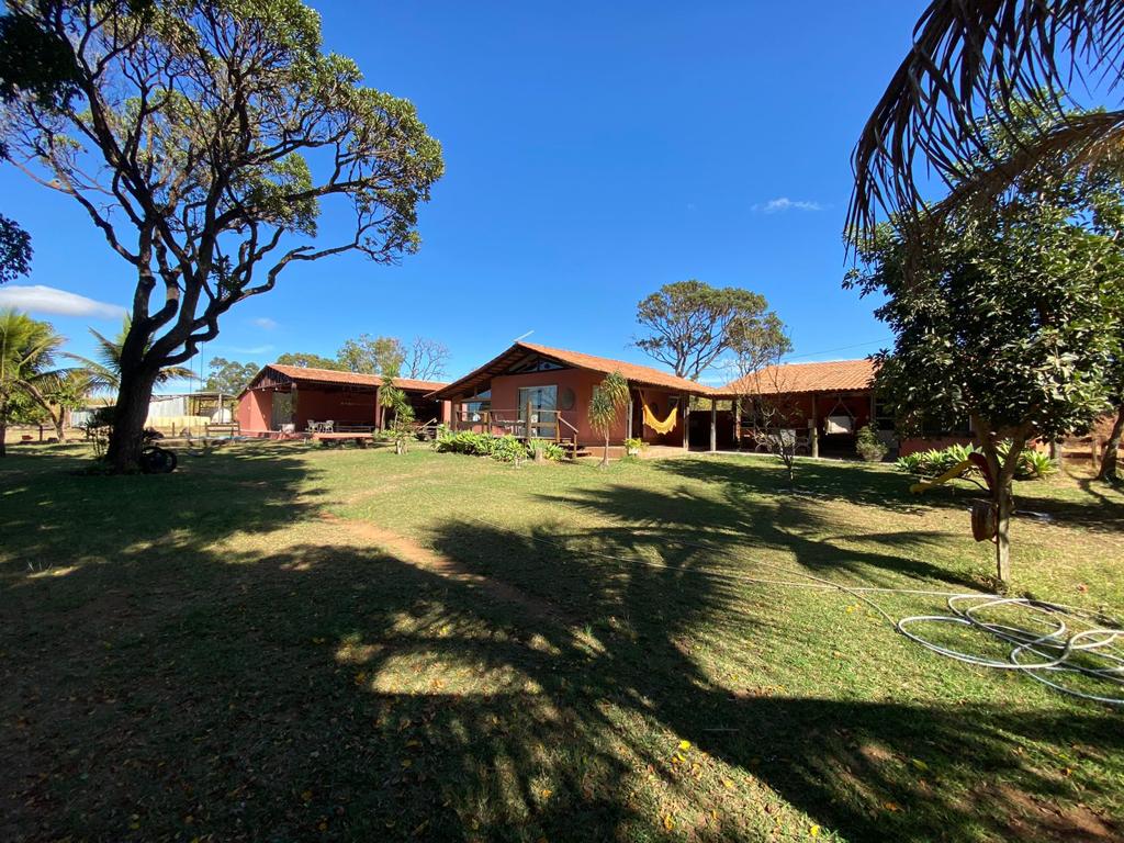 The exterior features a spacious garden area surrounded by various trees, providing shade and greenery. Two chalets are visible, showcasing traditional architecture with red walls and sloped roofs. A hammock is seen hanging in a relaxing spot, enhancing the tranquil outdoor setting.