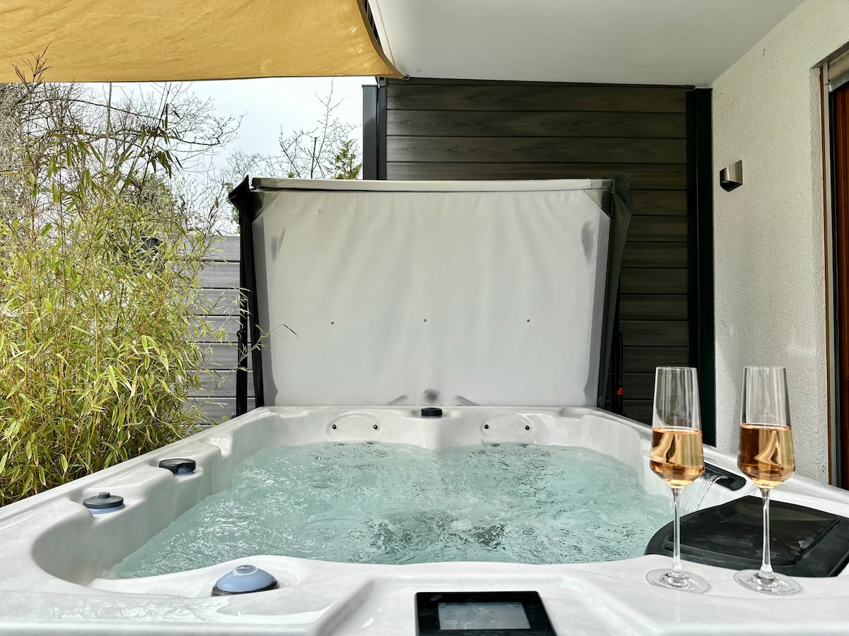 A private whirlpool is shown with bubbling water, surrounded by greenery. Two glasses of sparkling wine are placed on the edge, adding to the inviting ambiance. The area is partially shaded by a large awning, creating a relaxing atmosphere for enjoyment.