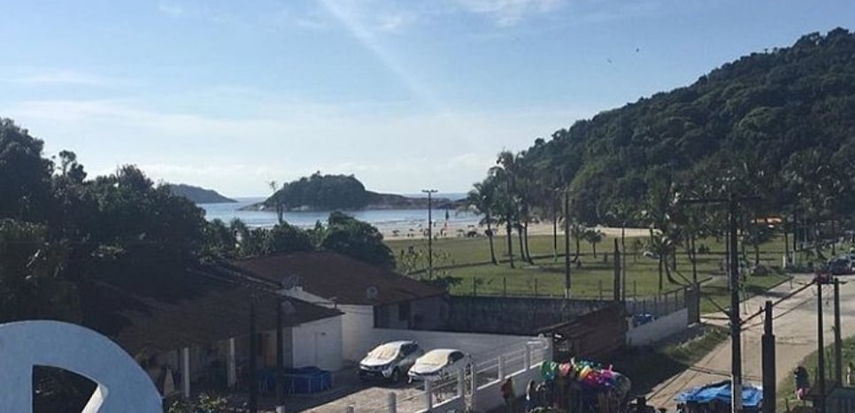 A scenic view of the beach is captured, showcasing soft sandy shores and gentle waves. Lush greenery lines the coastline, while small hills rise in the background. The area appears inviting, with a pathway leading towards the beach, enhancing the serene landscape.