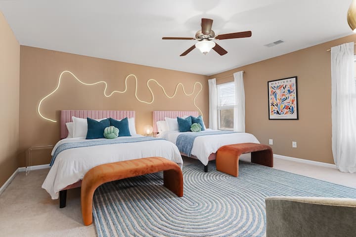 Descubre la comodidad y el estilo en este espacioso dormitorio, con dos camas tamaño queen adornadas con acogedoras sábanas, complementadas por la suave brisa de un ventilador de techo.