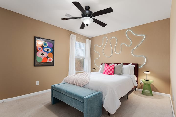 Empápate del encanto de este dormitorio ecléctico, donde las vibrantes exhibiciones se mezclan con lujosos muebles. Una acogedora cama queen, un elegante ventilador de techo y un lujoso taburete de extremo crean una mezcla armoniosa de comodidad y estética única.